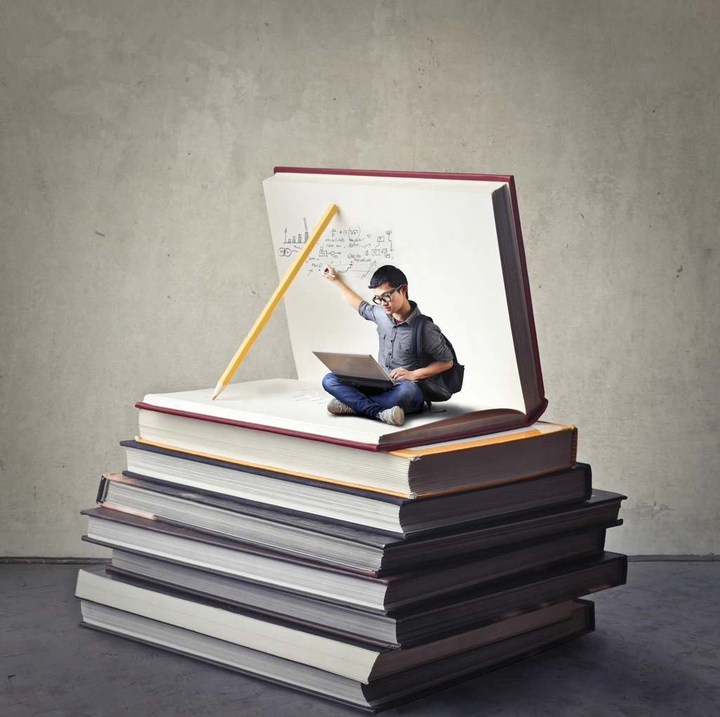 Schüler am Laptop sitzend auf einem Bücherstapel