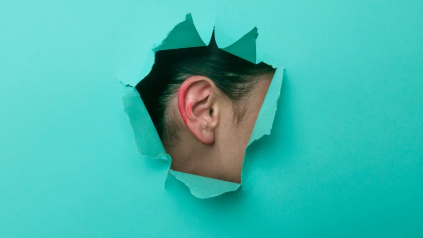 Female ear close-up. Copy space. Torn paper, blue background.