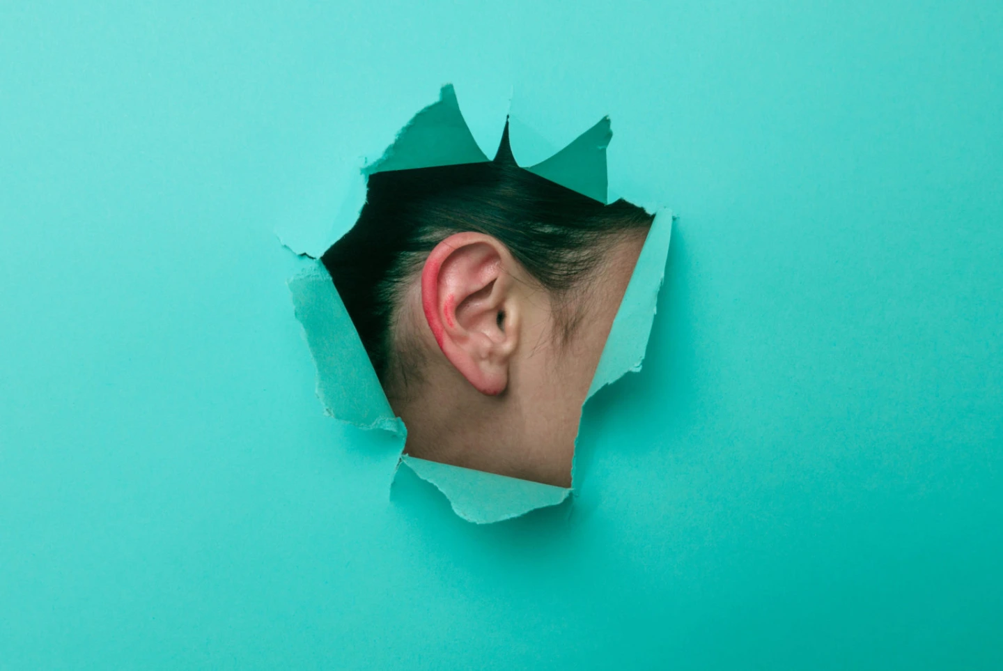 Female ear close-up. Copy space. Torn paper, blue background.