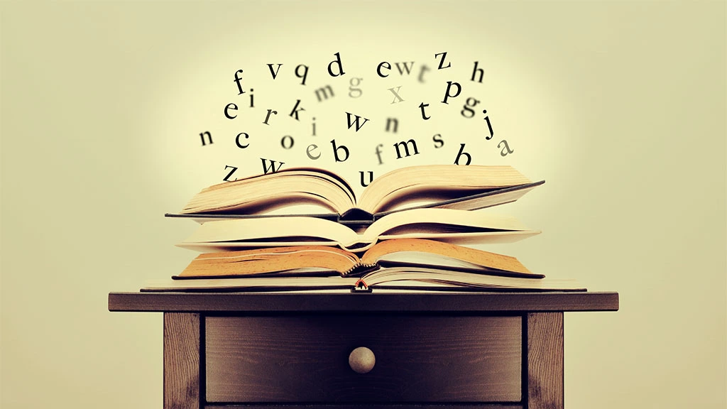 Symbolbild vier aufeinanderliegender geöffneter Bücher aus denen die Buchstaben fliegen