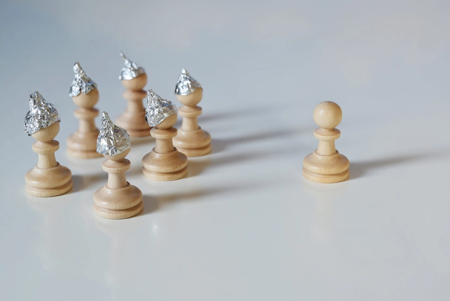 Group of pawn chess pieces with tinfoil hats against imagined heteronomy stand towards a piece without hat, conspiracy theory and manipulation concept in coronavirus time